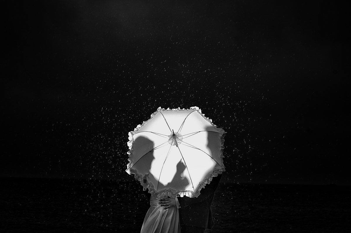 Hochzeitspaar in Regen versteckt hinter Regenschirm