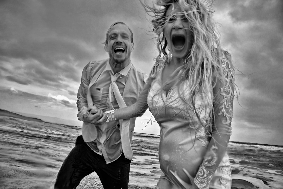 Eine durchgefrorene nasse und schwangere Braut und ihr Bräutigam direkt nach dem herbstlichen Fotoshooting aus dem Meer steigend.